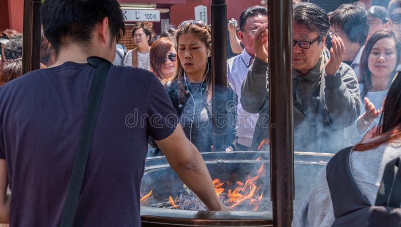 Tourists At Sensoji Temple Incense Burner, Tokyo, Japan. Tokyo, Japan - April 28th, 2017. Tourist drawing smoke believe to have healing properties from Jokoro or royalty free stock images